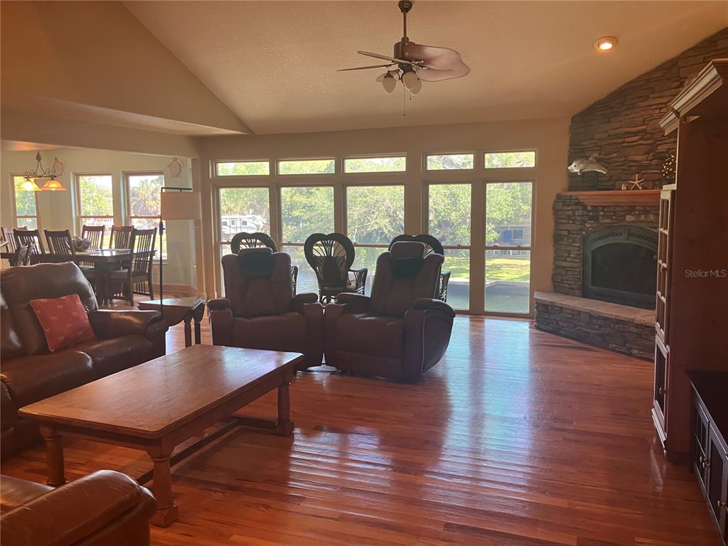 A living room features hardwood floors, a stone fireplace, and large windows overlooking a pool — 5361 CIRCLE DRIVE, WEEKI WACHEE, FL