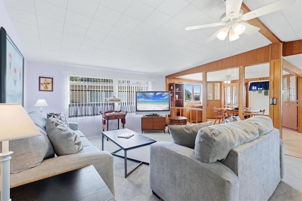 A living room features gray sofas, a television, wood-paneled walls, and a ceiling fan — 1419 41ST AVENUE E, ELLENTON, FL