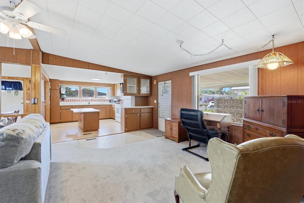 A living room with wood paneling, carpet, and an open kitchen with wooden cabinets — 1419 41ST AVENUE E, ELLENTON, FL