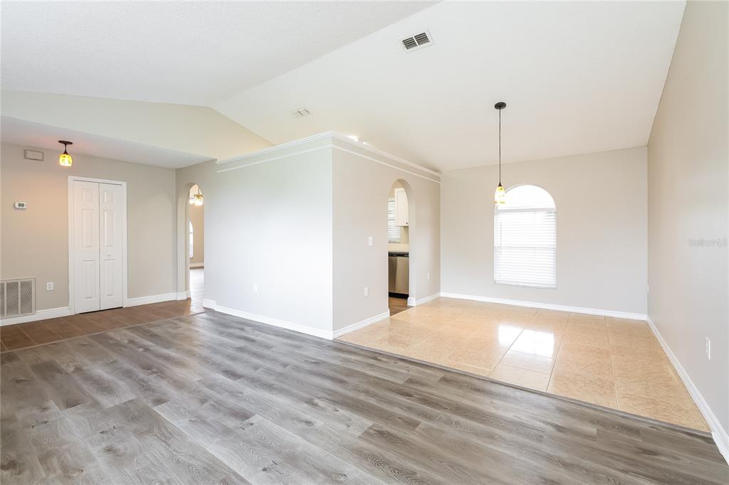 A living area with wood-look flooring transitions to a tiled dining space with an arched window — 817 ALBI COURT, KISSIMMEE, FL