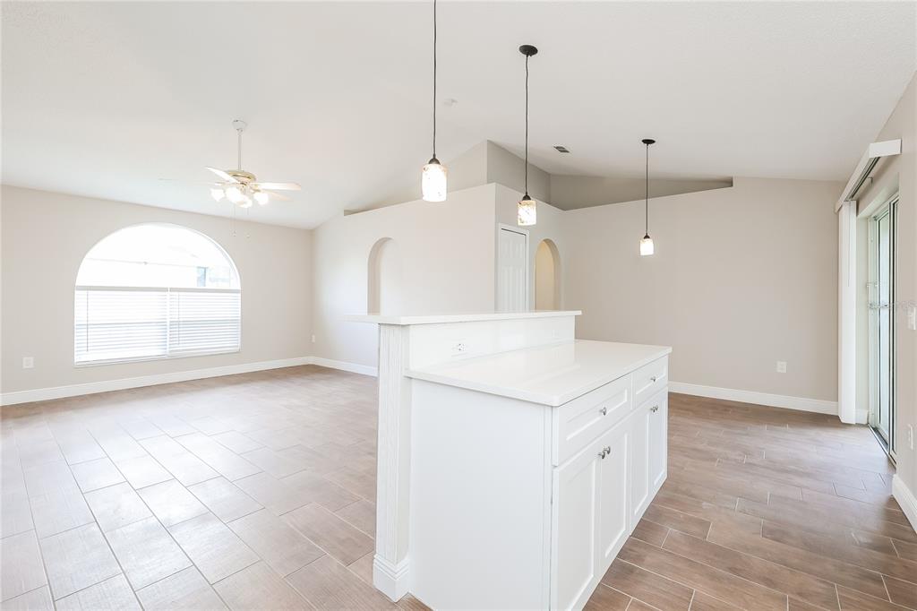 A bright, open-concept living area features tile flooring, a white kitchen island, and arched doorways — 817 ALBI COURT, KISSIMMEE, FL