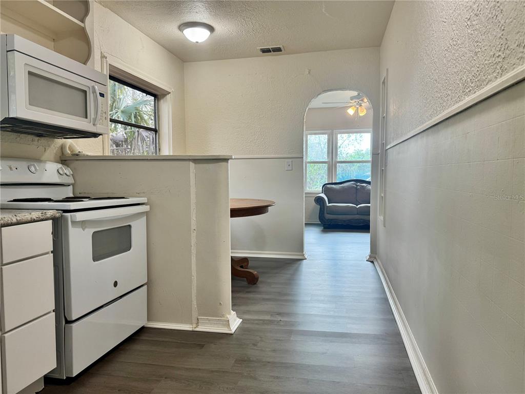 A kitchen with white appliances and wood-look flooring opens into a living area beyond — 425 E SESSOMS AVENUE, LAKE WALES, FL
