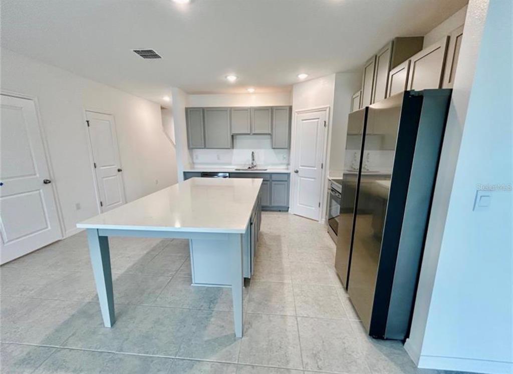 A kitchen features a large white island, gray cabinets, stainless steel appliances, and tile flooring — 10759 IRONWOOD TREE WAY, SAN ANTONIO, FL