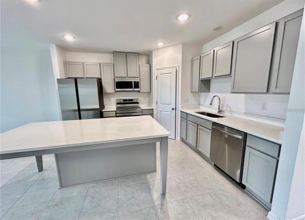A modern kitchen features gray cabinets, stainless steel appliances, a large island, and tile flooring — 10759 IRONWOOD TREE WAY, SAN ANTONIO, FL