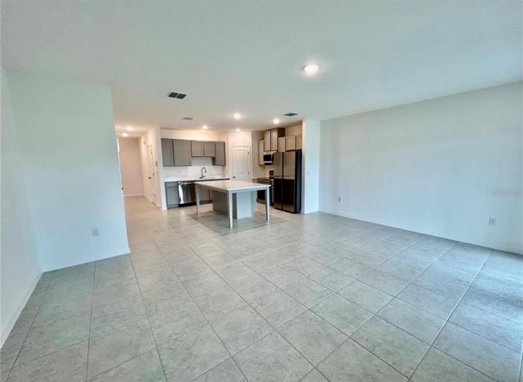 An open-concept kitchen with a central island and gray cabinetry sits adjacent to a tiled living area — 10759 IRONWOOD TREE WAY, SAN ANTONIO, FL