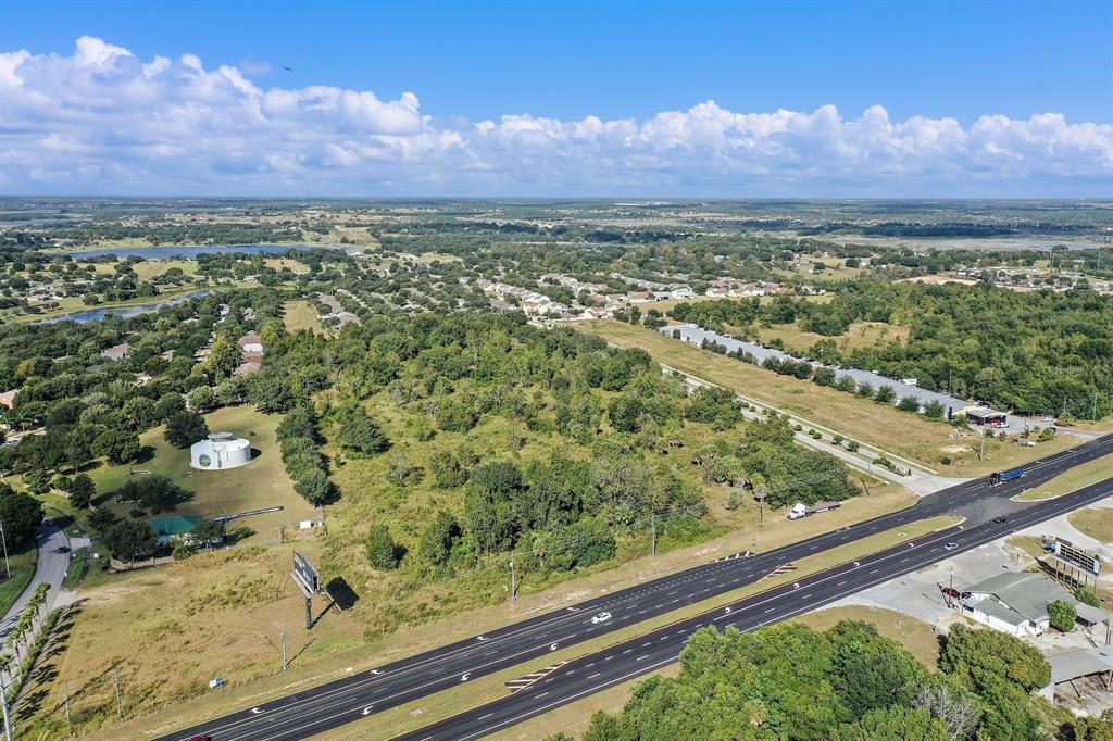 An aerial view shows a multi-lane highway bordering a large, wooded plot of undeveloped land — 17545 US HWY 27, MINNEOLA, FL