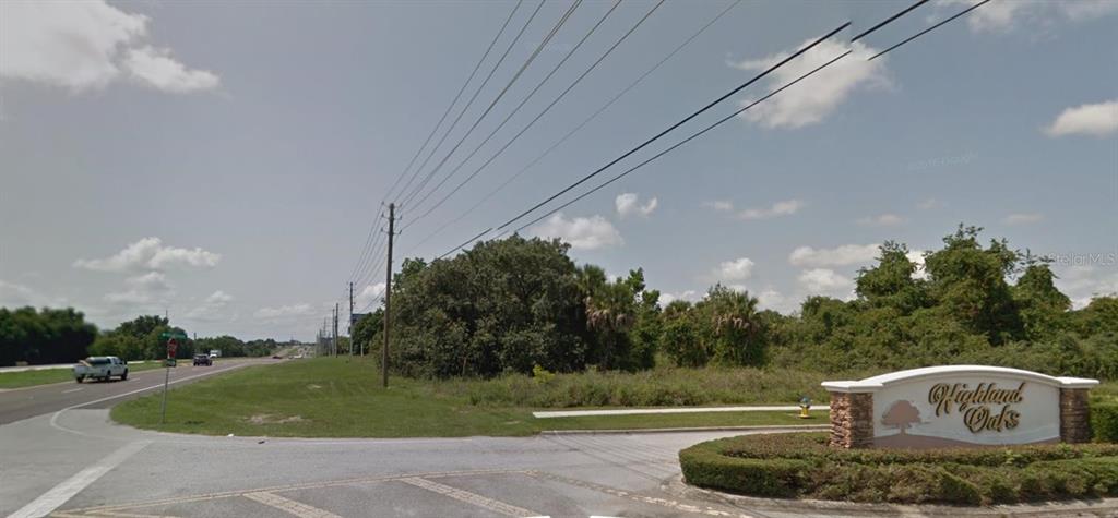 A stone entrance sign for Highland Oaks stands beside a road with power lines overhead — 17545 US HWY 27, MINNEOLA, FL