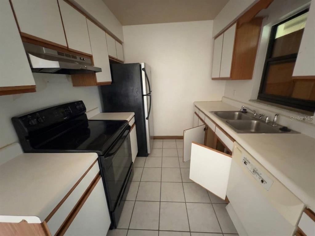 A galley-style kitchen features white cabinets, black appliances, a double sink, and tiled flooring — 996 GRAYSON DRIVE, ORLANDO, FL