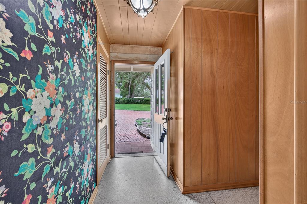 An entryway features floral wallpaper, wood paneling, a light fixture, and an open door to outdoors — 2435 BROADVUE AVE, EUSTIS, FL