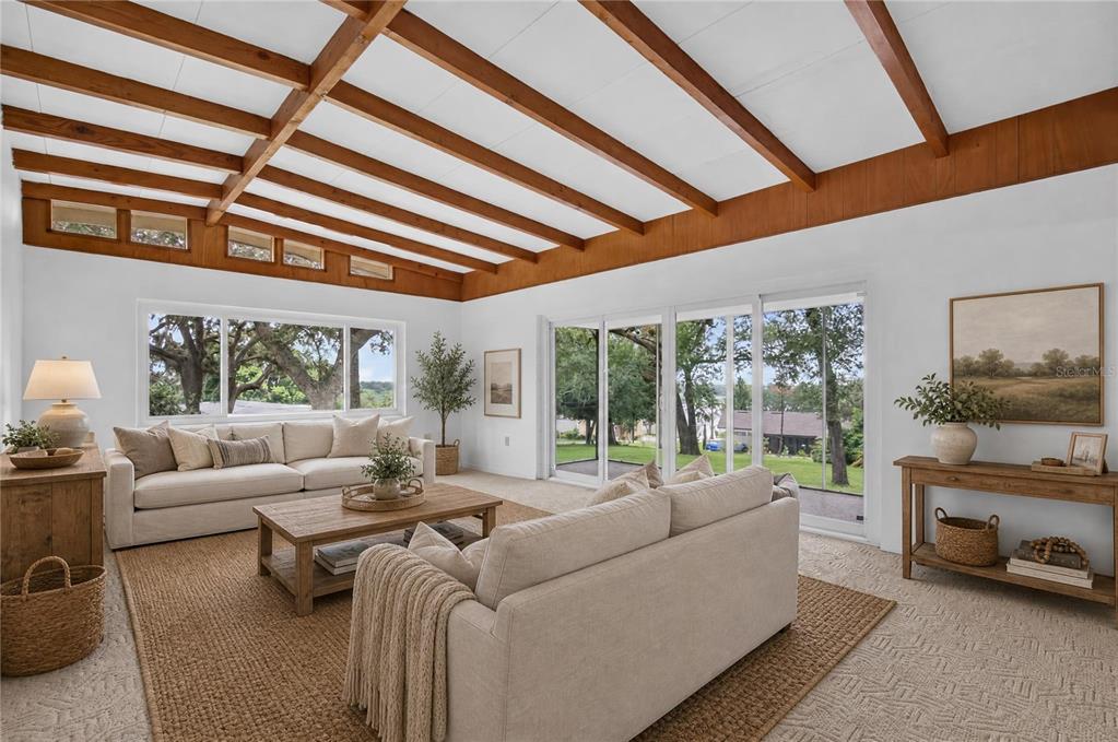 A living room features a beamed ceiling, large windows, sliding glass doors, and neutral furniture — 2435 BROADVUE AVE, EUSTIS, FL