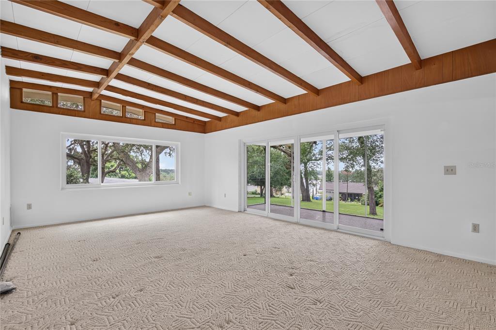 A living room with beige carpet, exposed wood ceiling beams, and large windows and doors — 2435 BROADVUE AVE, EUSTIS, FL
