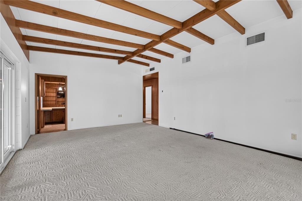 An empty living room features a vaulted ceiling with exposed wooden beams and beige carpeting — 2435 BROADVUE AVE, EUSTIS, FL