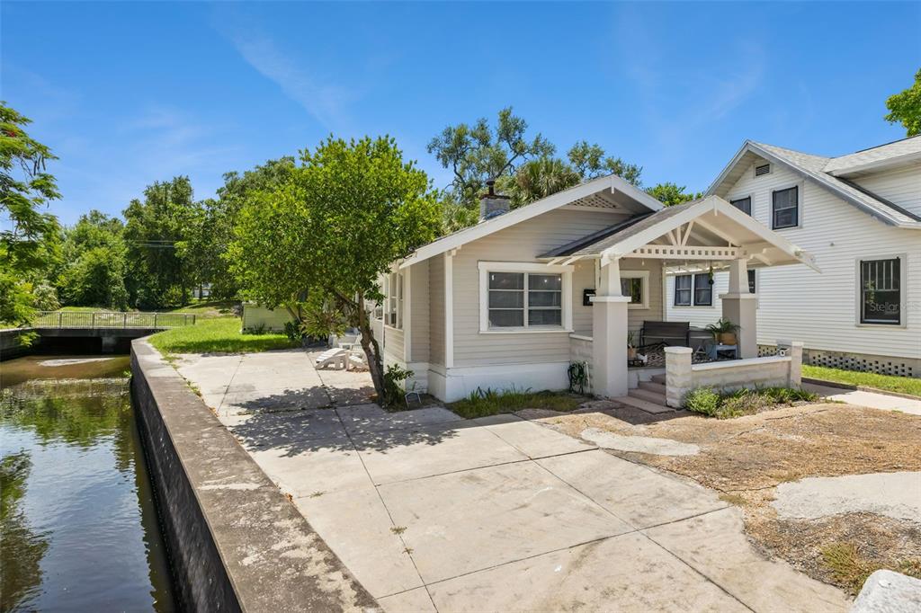A light-colored bungalow with a front porch sits next to a concrete-lined canal — 558 10TH AVE S, ST PETERSBURG, FL