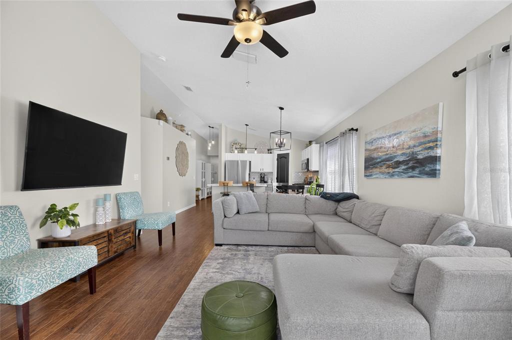 A living room with a sectional sofa, television, and open kitchen in the background — 7629 DEVONBRIDGE GARDEN WAY, APOLLO BEACH, FL