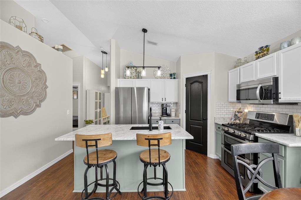 A kitchen features a marble-topped island, light green cabinetry, stainless steel appliances, and wood flooring — 7629 DEVONBRIDGE GARDEN WAY, APOLLO BEACH, FL