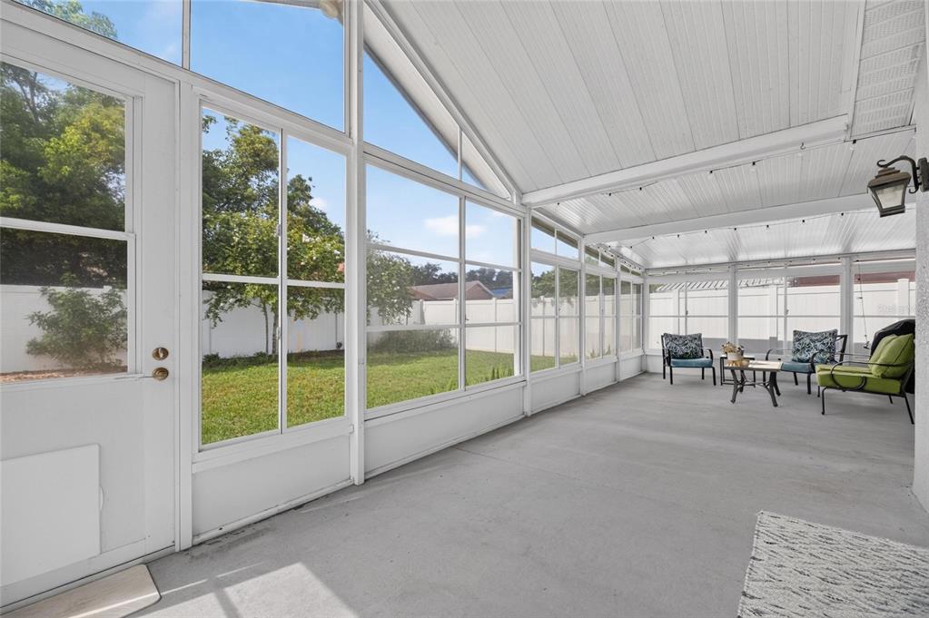A bright, enclosed sunroom features a concrete floor, white framing, and views of a backyard — 7629 DEVONBRIDGE GARDEN WAY, APOLLO BEACH, FL