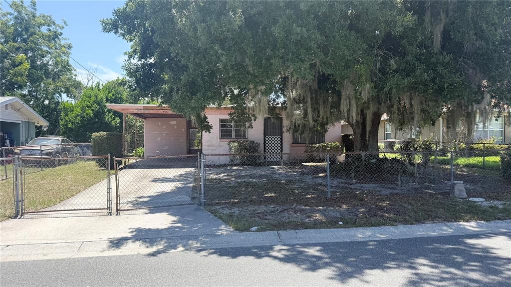 A single-story pink house with a carport sits behind a chain-link fence and large tree — 1903 3RD STREET NE, WINTER HAVEN, FL