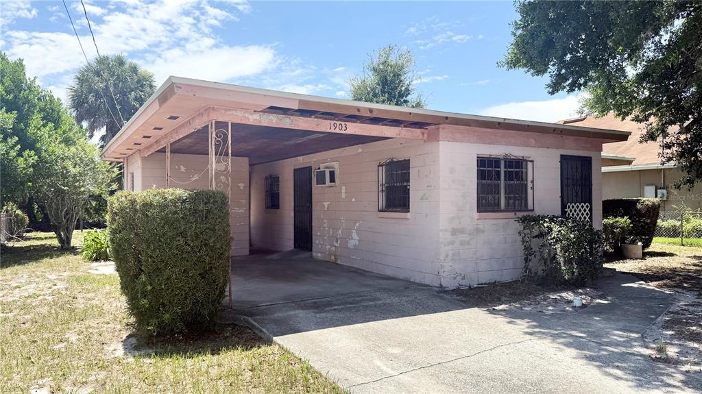 A single-story pink concrete block house features a carport and barred windows — 1903 3RD STREET NE, WINTER HAVEN, FL