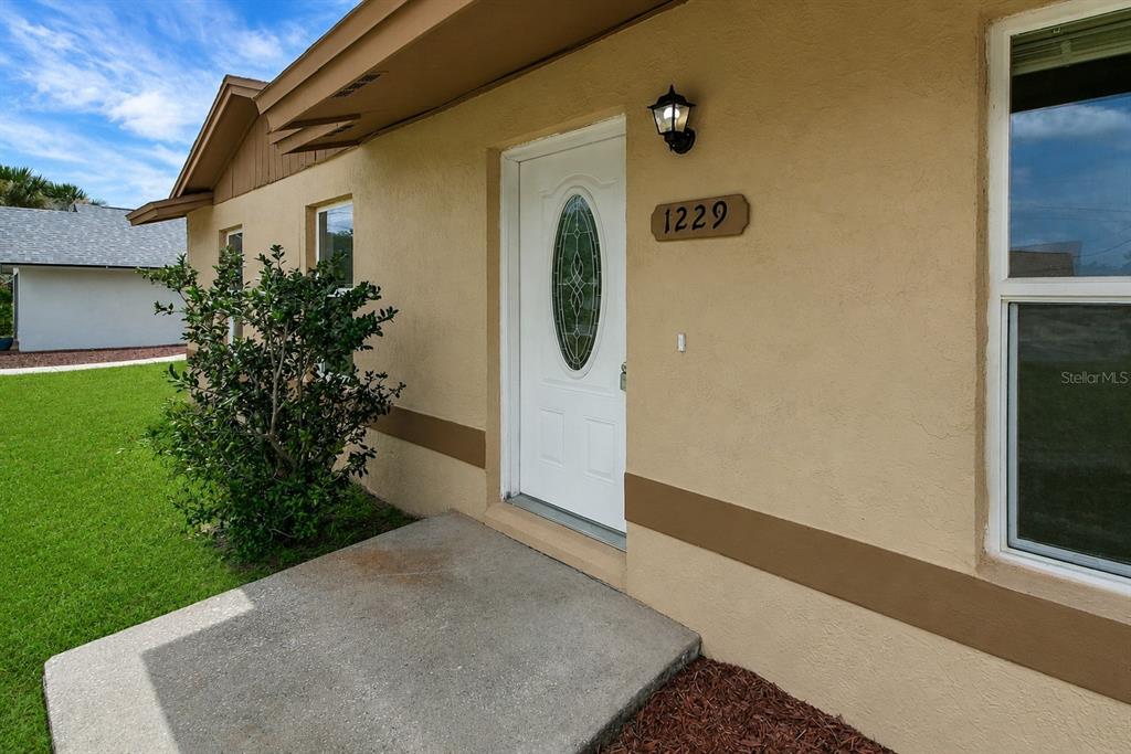 The exterior of a tan house features a white front door and a concrete porch — 1229 PADGETT CIRCLE, LADY LAKE, FL