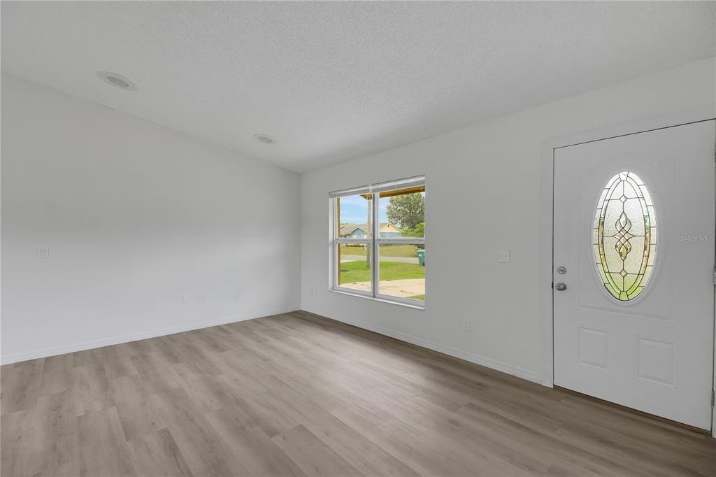 An empty room with white walls, light wood-look flooring, a window, and a front door — 1229 PADGETT CIRCLE, LADY LAKE, FL