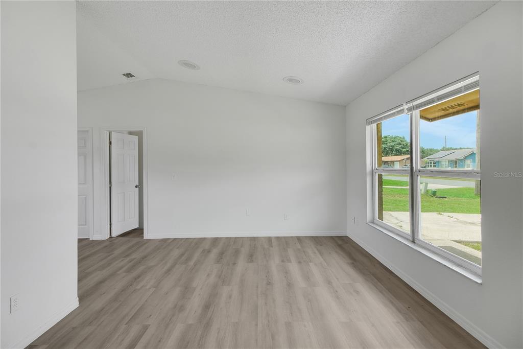 An empty room with light wood-look flooring, white walls, recessed lighting, and a large window — 1229 PADGETT CIRCLE, LADY LAKE, FL