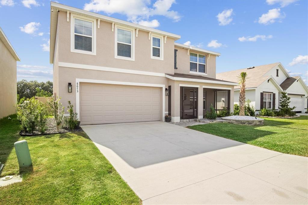 A two-story suburban house features a beige stucco exterior, a two-car garage, and a porch — 8673 TRIUMPH CIRCLE, WILDWOOD, FL
