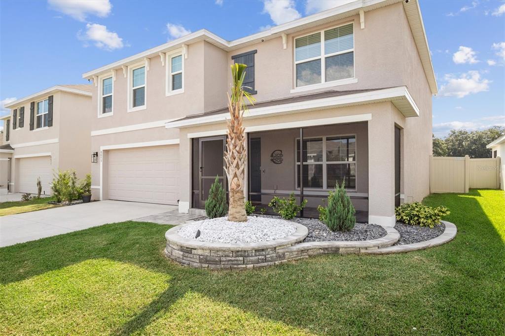 A two-story suburban house features a screened front porch, a palm tree, and a driveway — 8673 TRIUMPH CIRCLE, WILDWOOD, FL