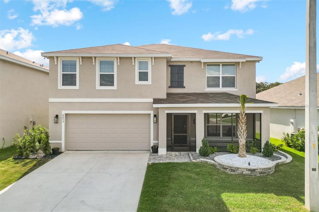 A two-story suburban house with a beige stucco exterior, a two-car garage, and a screened porch — 8673 TRIUMPH CIRCLE, WILDWOOD, FL