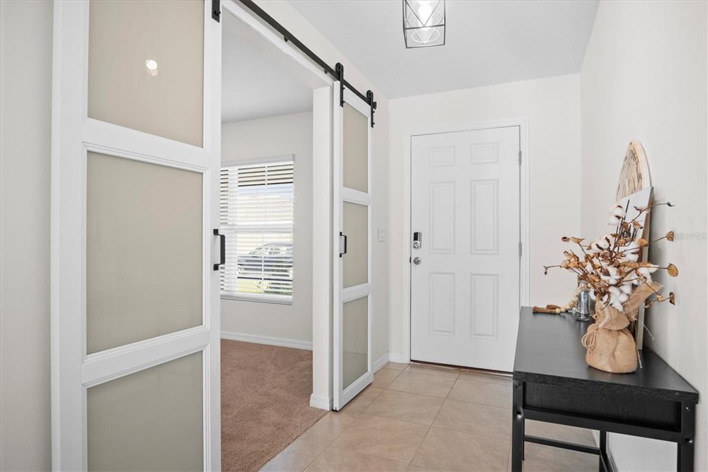 An entryway features tile flooring, a white front door, and sliding glass barn doors — 8673 TRIUMPH CIRCLE, WILDWOOD, FL