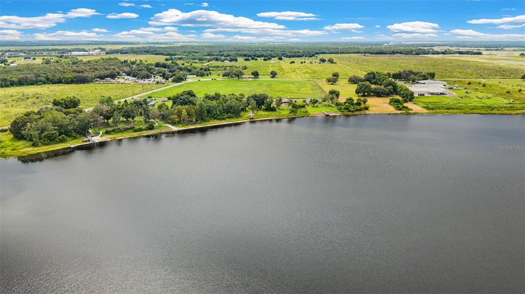 An aerial view shows a large lake bordered by grassy fields, trees, and several buildings — 930 ALBRITTON WAY, LAKE WALES, FL