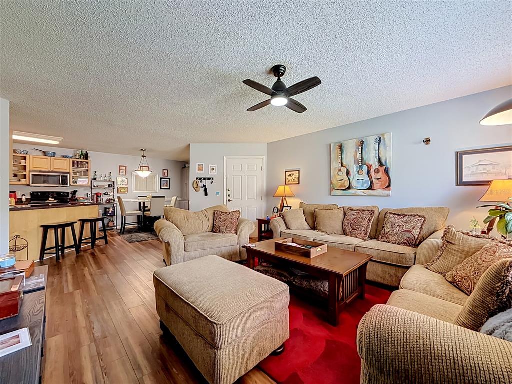 A living room with wood-look flooring, a red area rug, and an open kitchen — 1550 S BELCHER ROAD UNIT 214, CLEARWATER, FL