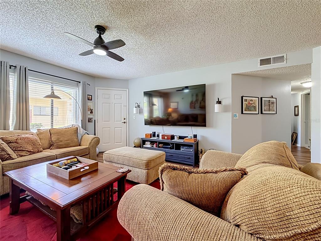 A living room features a textured ceiling, a ceiling fan, a television, and tan furniture — 1550 S BELCHER ROAD UNIT 214, CLEARWATER, FL