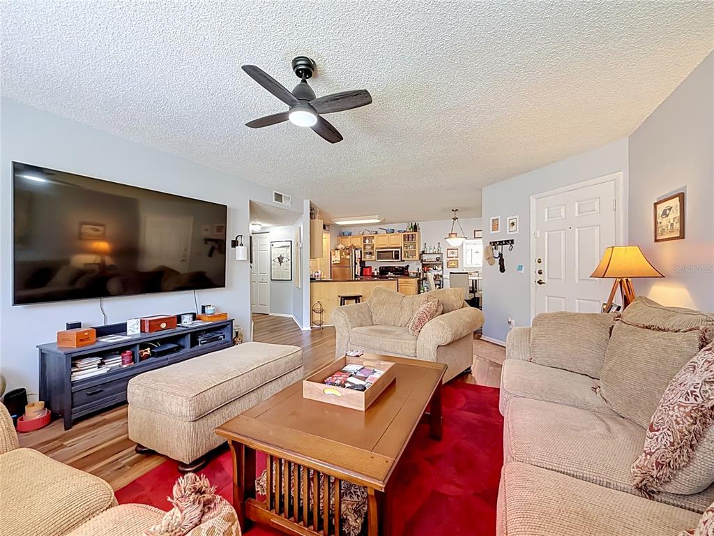 A living room features a large television, beige upholstered furniture, and a red area rug — 1550 S BELCHER ROAD UNIT 214, CLEARWATER, FL