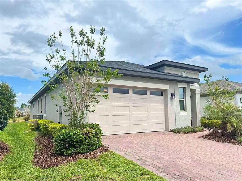 A single-story house exterior features a beige garage door, a brick driveway, and landscaping — 3434 SAGEBRUSH STREET, HARMONY, FL