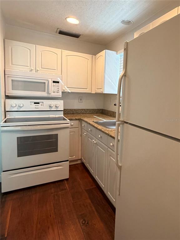 A kitchen features white cabinets, stainless steel appliances, granite countertops, and dark wood flooring — 415 CELEBRATION AVENUE UNIT B, CELEBRATION, FL