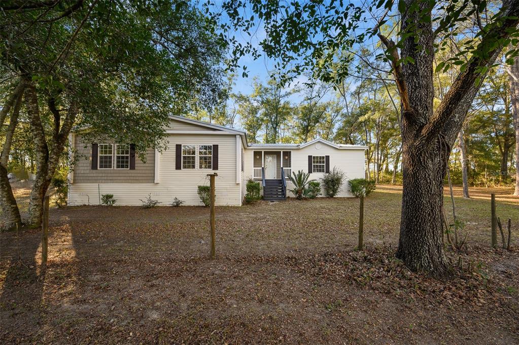 A single-story house with light siding and a front porch sits on a wooded lot — 13076 SW 154TH STREET, ARCHER, FL