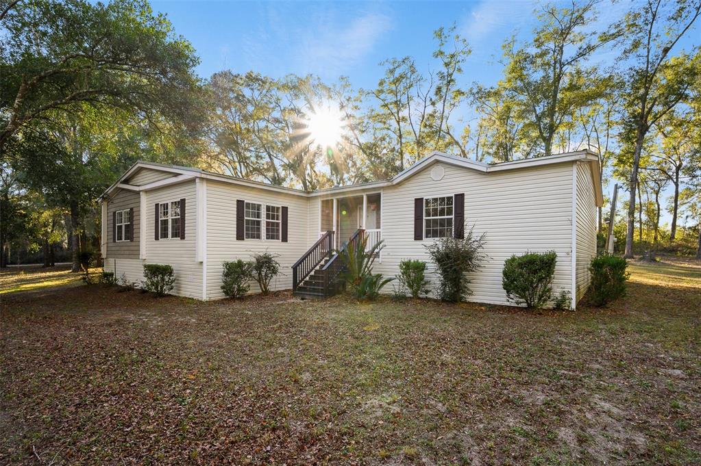 A light-colored manufactured home with a recessed entrance and dark shutters sits on a lot — 13076 SW 154TH STREET, ARCHER, FL