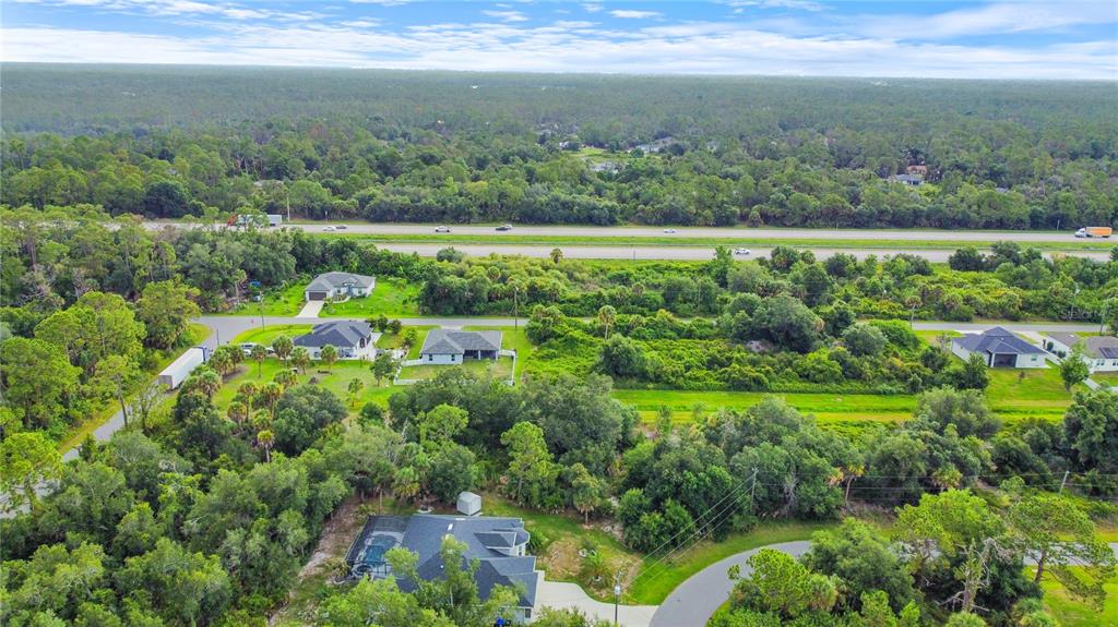 An aerial view shows several houses surrounded by dense trees near a multi-lane highway — ANCIENT ROAD, NORTH PORT, FL