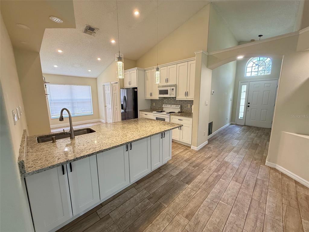 A kitchen features white cabinetry, granite countertops, a large island, and wood-look tile flooring — 1221 SINGLETON CIRCLE, GROVELAND, FL