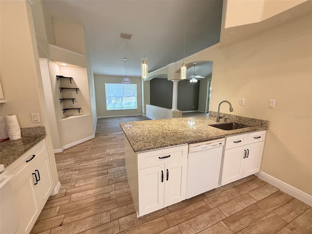 A kitchen with white cabinets, granite countertops, and wood-look tile flooring opens to a living area — 1221 SINGLETON CIRCLE, GROVELAND, FL