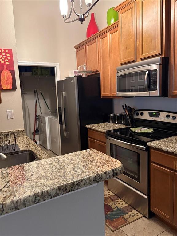 A kitchen features wood cabinets, granite countertops, stainless steel appliances, and an adjacent laundry closet — 2516 GRASSY POINT DRIVE UNIT 200, LAKE MARY, FL