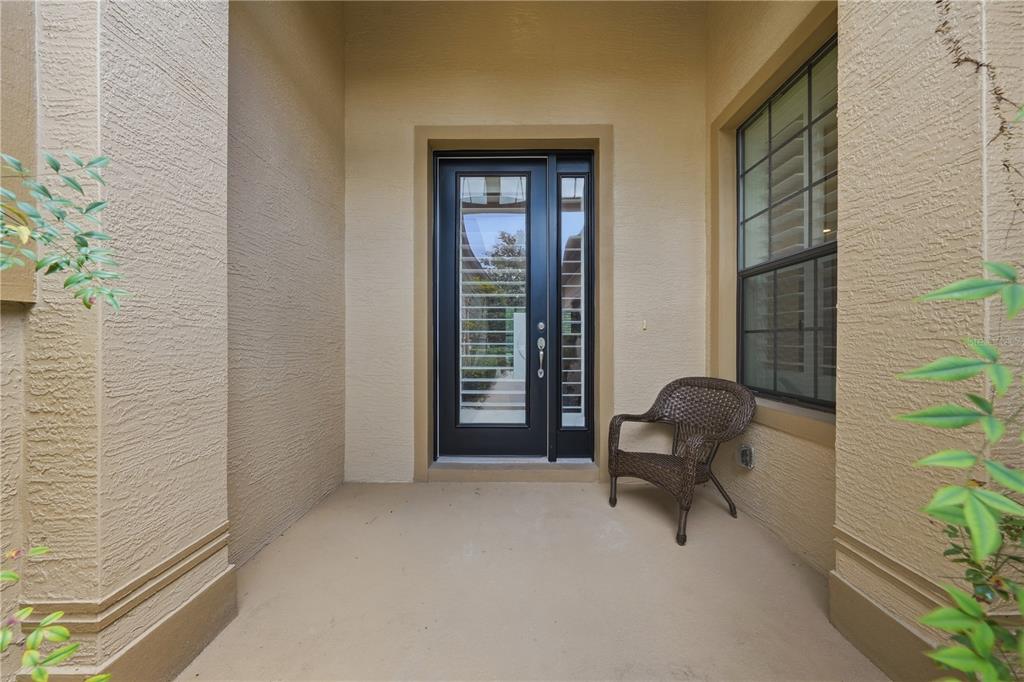 A covered entryway features a dark front door with glass panels and a wicker chair — 1031 KILKENNY LANE, ORMOND BEACH, FL