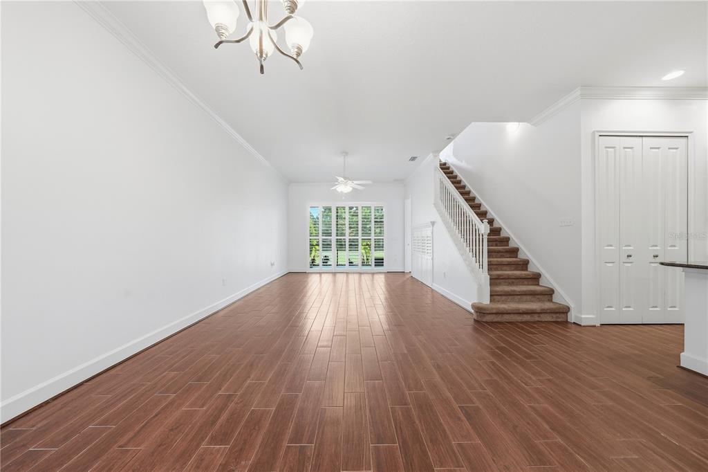 An empty living room features wood-look tile flooring, white walls, and a carpeted staircase — 1031 KILKENNY LANE, ORMOND BEACH, FL