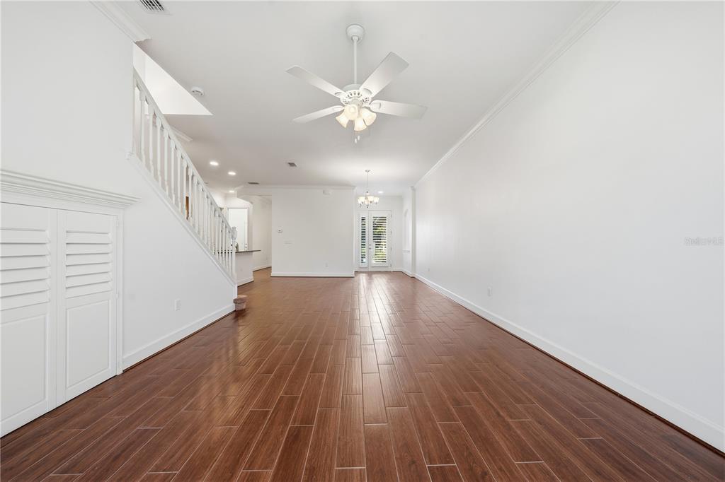 A long, empty room features white walls, wood-look tile flooring, a ceiling fan, and a staircase — 1031 KILKENNY LANE, ORMOND BEACH, FL