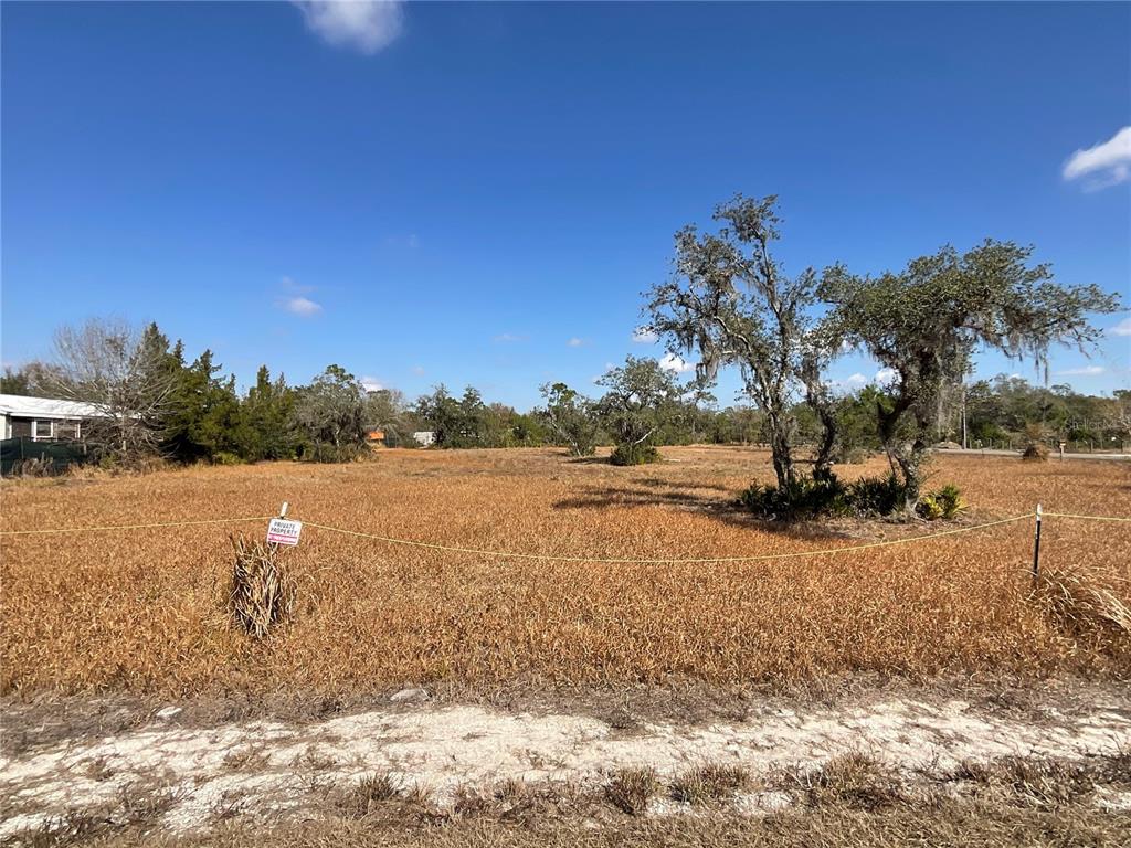 A vacant, grassy lot features a private property sign and several mature trees — 490 HOBBS DRIVE, VENUS, FL