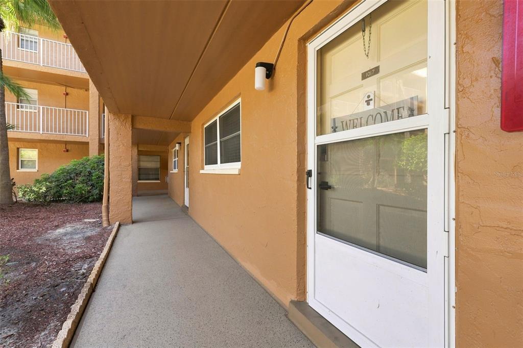 An exterior view of a ground-floor apartment entrance with a walkway and tan stucco walls — 12760 INDIAN ROCKS ROAD UNIT 1017, LARGO, FL