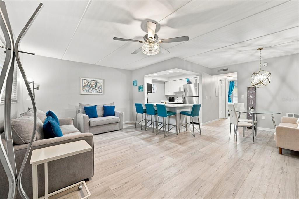 An open-concept living and dining area features light wood flooring, blue accents, and a kitchen — 12760 INDIAN ROCKS ROAD UNIT 1017, LARGO, FL
