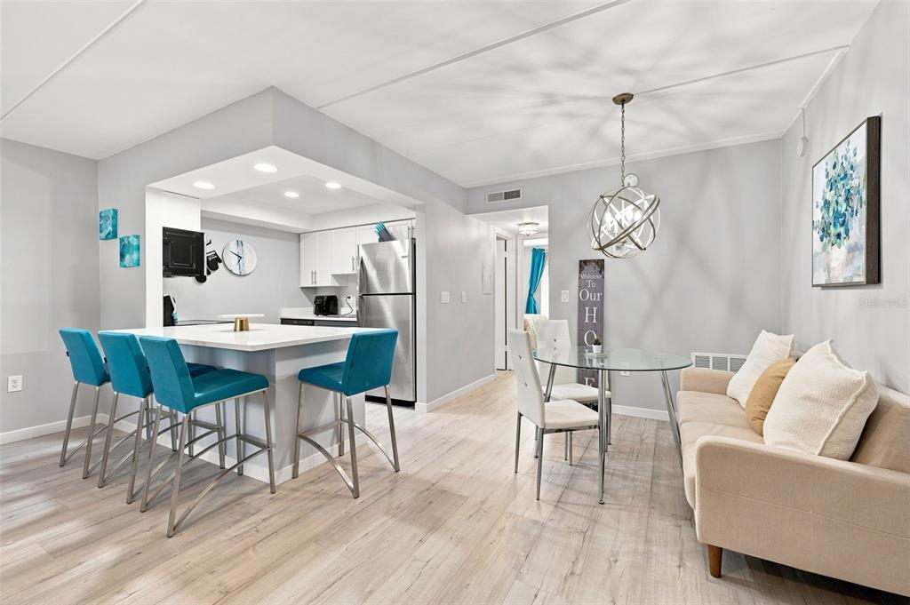 A kitchen with a breakfast bar and dining area featuring light wood floors and gray walls — 12760 INDIAN ROCKS ROAD UNIT 1017, LARGO, FL