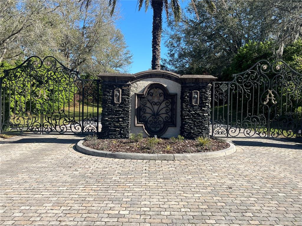 A stone pillar with a decorative metal insert stands between two large wrought iron gates — 000 SE 118TH LANE, BELLEVIEW, FL