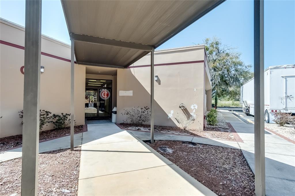 A covered walkway leads to the entrance of a beige commercial building with a glass door — 6801 US 27 HIGHWAY N UNIT C4, SEBRING, FL